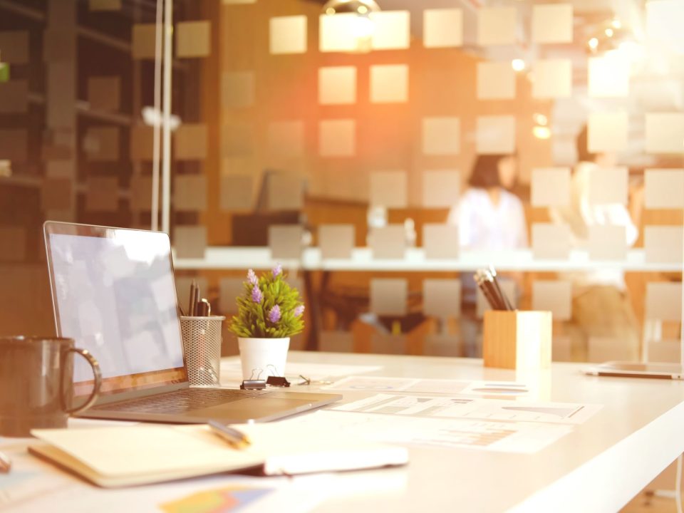 Arbeitsplatz mit Laptop, Kaffeebecher und Notizblock in einem hellen Büro